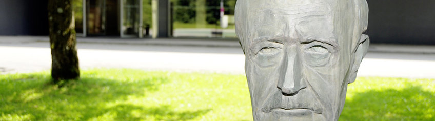 Photo with part of the institute's entrance in the background and the Max Planck face (statue) up close.